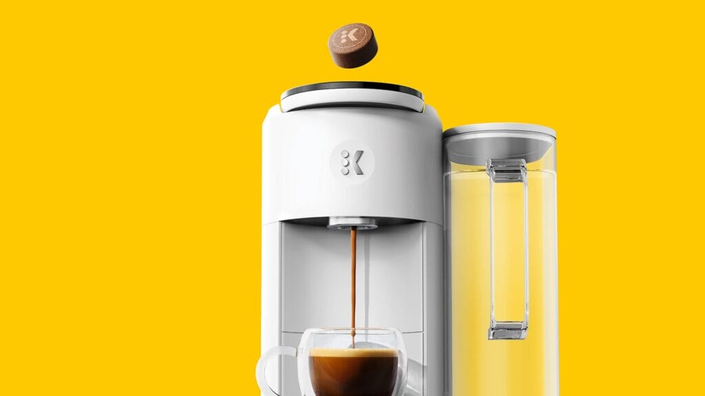 Keurig Next-Generation capsule k-round coffee machine with a glass of coffee on a yellow background.