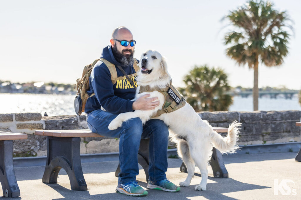 Man sitting on a bench celebrates with a happy dog, a milestone achievement from K9s For Warriors.