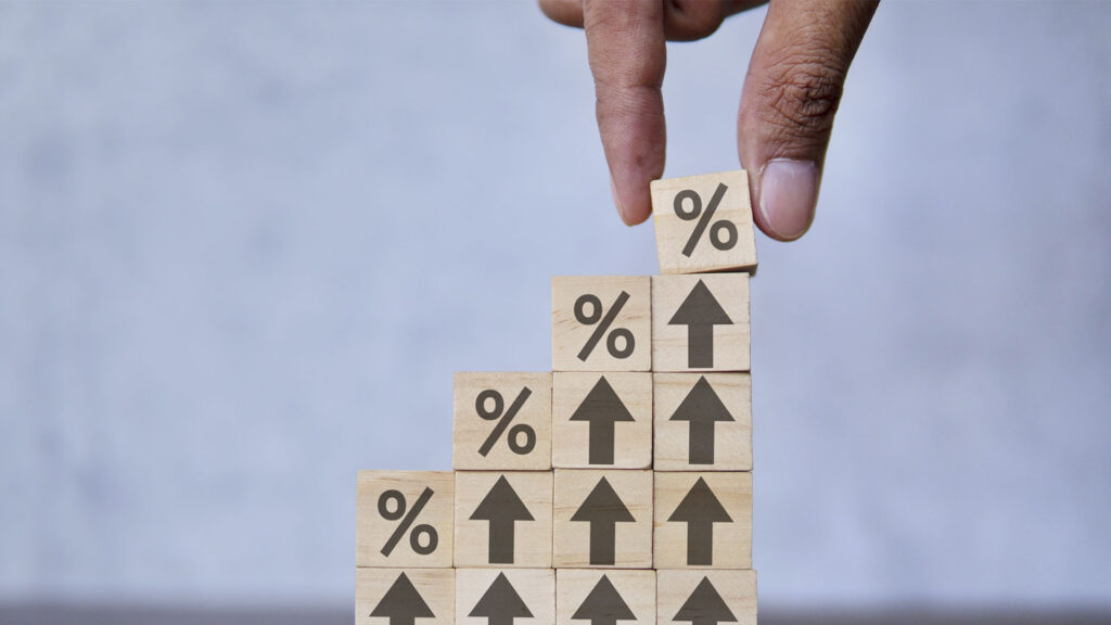 A hand places a wooden block with a percentage symbol on top of a staircase of blocks featuring percentage symbols and upward arrows, questioning if renting is ruining your future.