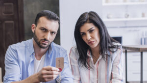 A man and woman sit together in a bright kitchen, both with serious expressions, holding a key labeled "for sale." Is renting ruining your future?