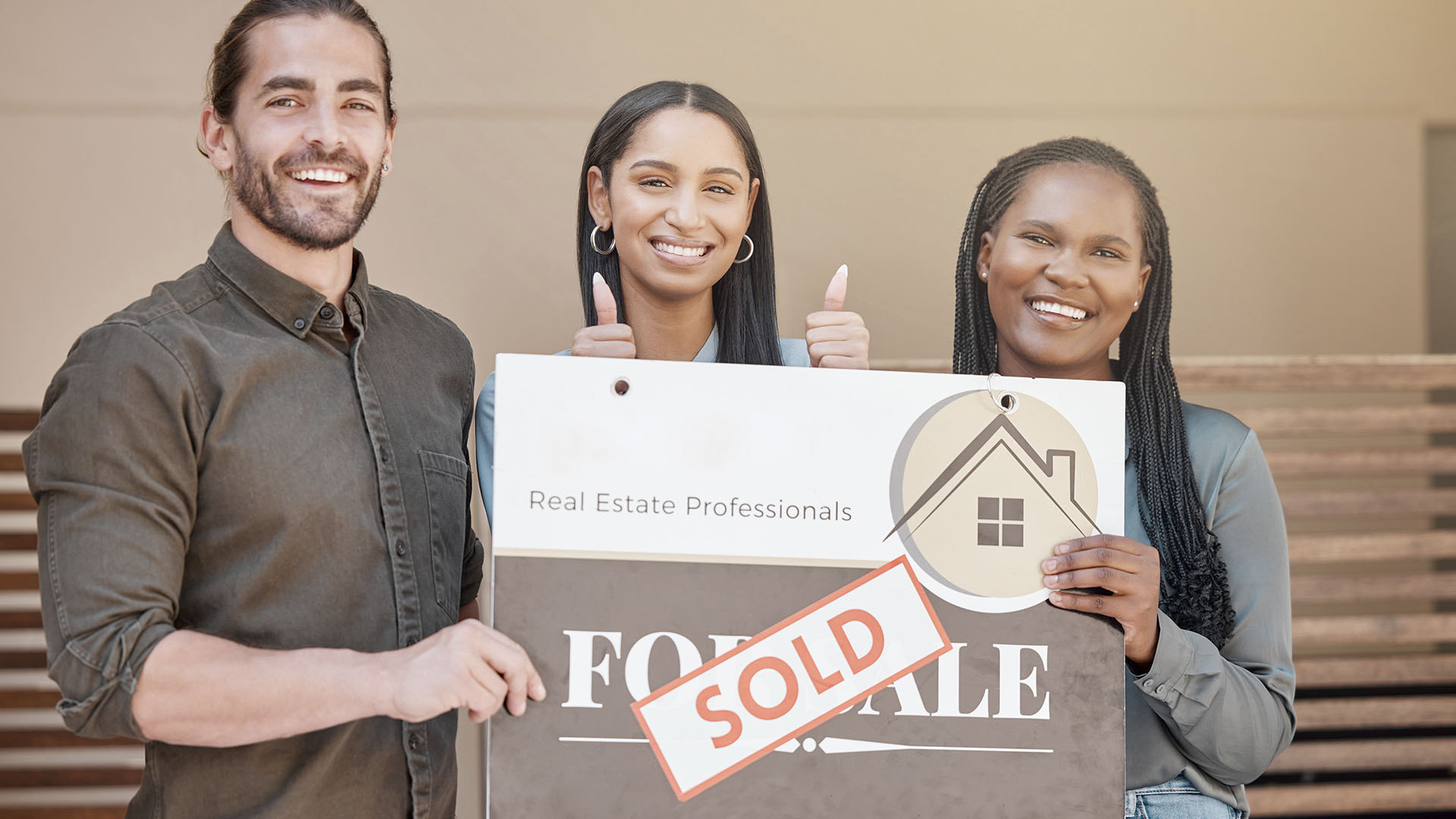 Three people happily holding a "For Sale" sign with a "Sold" sticker on it. They stand outside, smiling at the camera, as if to say, "Is renting ruining your future? Make the switch to homeownership today!