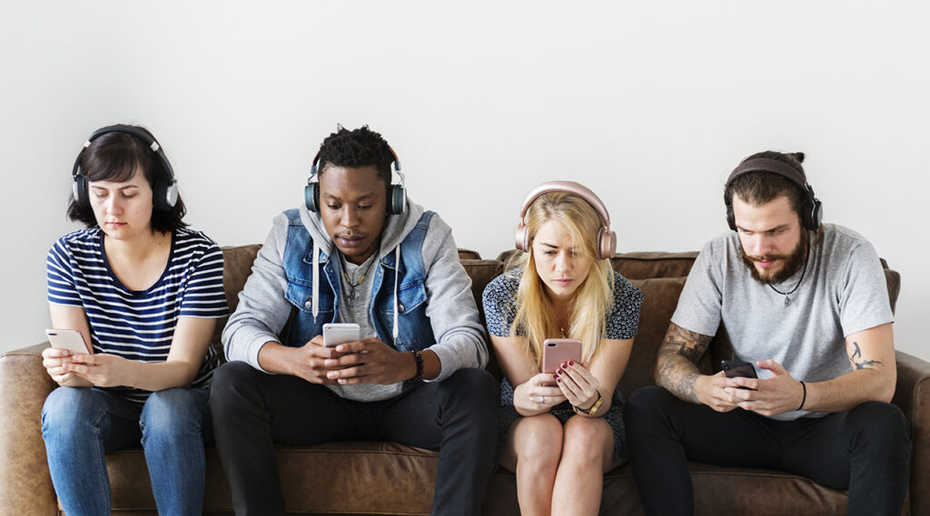 Four people sit on a couch, each wearing headphones and looking at their smartphones, seemingly at a breaking point in America's mental health crisis.