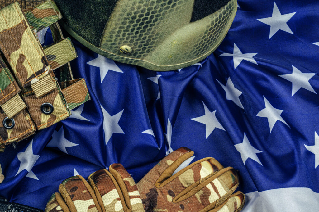 A military helmet, tactical vest, and gloves rest on a crumpled American flag with white stars on a blue background, symbolizing the dedication honored by the nation’s top Military Friendly Companies.