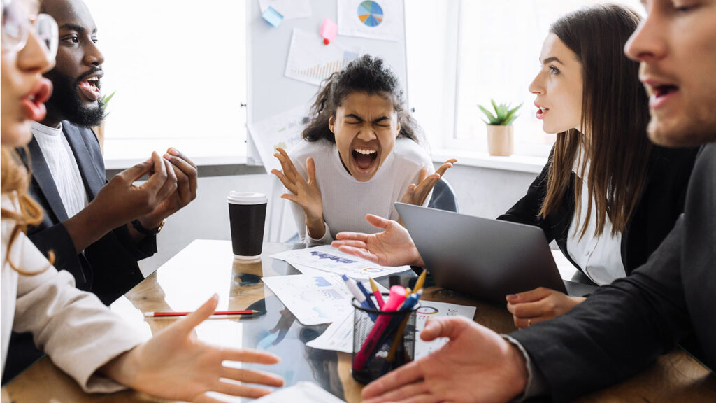 A group of people sits around a table having an intense discussion about the FTC Noncompete Ban. A young woman at the center appears stressed, holding her head and closing her eyes. Documents and a laptop are spread on the table.