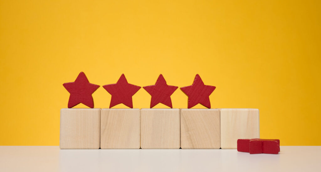 Feeling overwhelmed by fake reviews? Brighten your day with this charming scene: four red star-shaped blocks placed on four wooden cubes against a yellow background, accompanied by two additional red blocks resting on the white surface beside them.