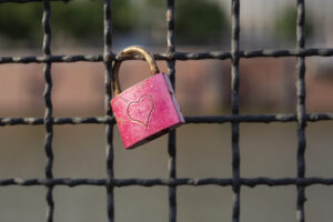 A pink padlock with a heart design is attached to a wire fence, holding on to your TikTok-worthy moment.