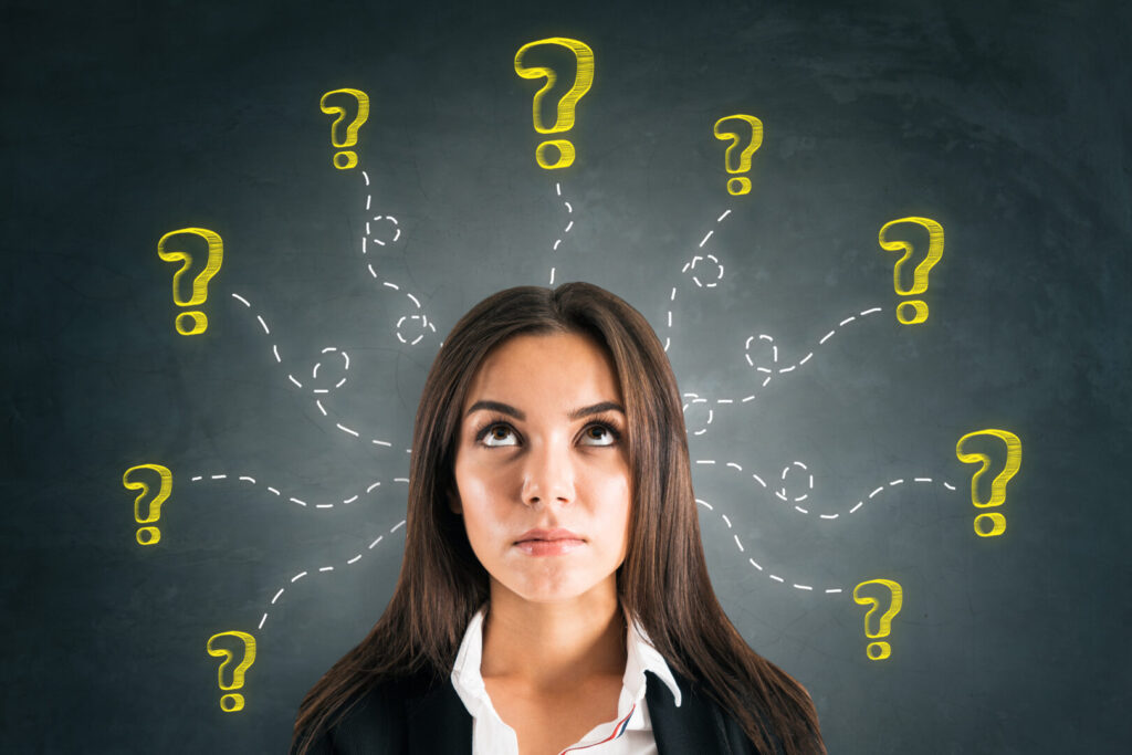 A woman looks upward with a thoughtful expression, surrounded by multiple yellow question marks drawn on a blackboard behind her, evoking curiosity about geography and earth sciences.