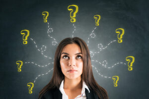 A woman looks upward with a thoughtful expression, surrounded by multiple yellow question marks drawn on a blackboard behind her, evoking curiosity about geography and earth sciences.